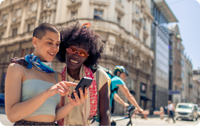 Dos mujeres sonríen y miran un teléfono juntas